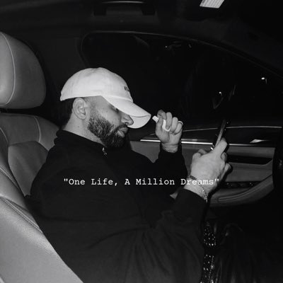 A black-and-white photo shows a bearded man in a white cap sitting in a car at night, holding what appears to be a small white object while looking at his phone. The caption reads **"One Life, A Million Dreams"** in white text across the image. The image fits the post's theme as it captures a candid, late-night moment that complements the feel-good vibe of the user randomly sending $4 ($SOL) to selected wallet addresses via Xpickr.