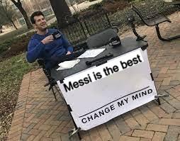 A man sits at a table with a sign reading 'Messi is the best / CHANGE MY MIND', a play on the popular meme format, while holding a pen and papers in a park.