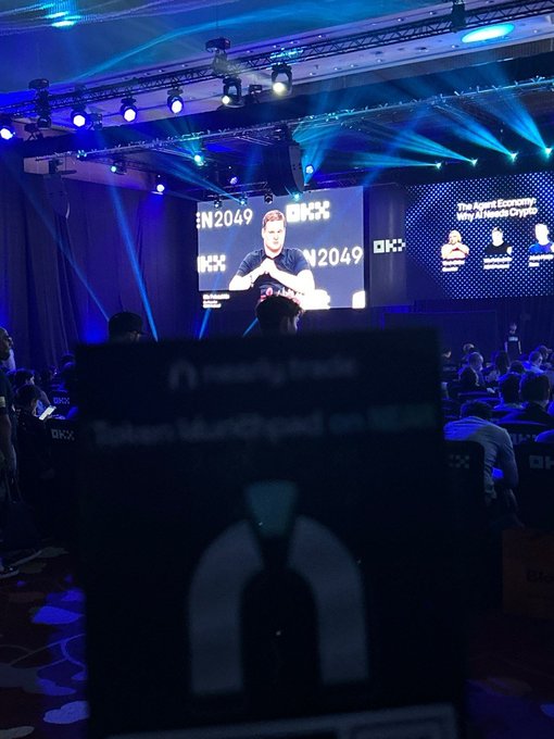 Interior view of the HKX conference, showing a large screen displaying a speaker with '2049' branding and the panel topic 'The Agent Economy: Why AI Needs Crypto.'
