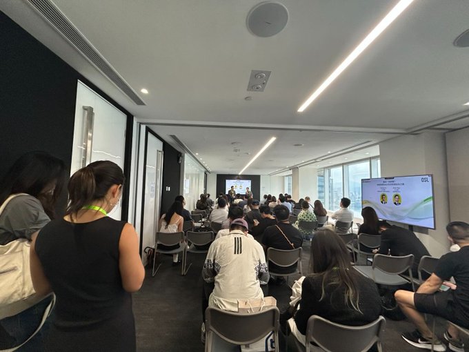 An audience sits in a modern conference room facing a presentation screen, with attendees viewing slides on a large display showing the 'BGL' logo.