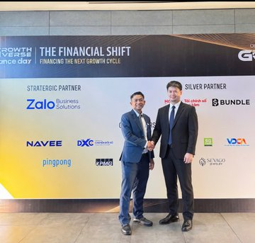 Two men in suits shaking hands at 'The Financial Shift' event, posing in front of a sponsor board featuring Zalo, Bundle, Navee, DXC, PingPong, Citibank, Visa, and SNVC.