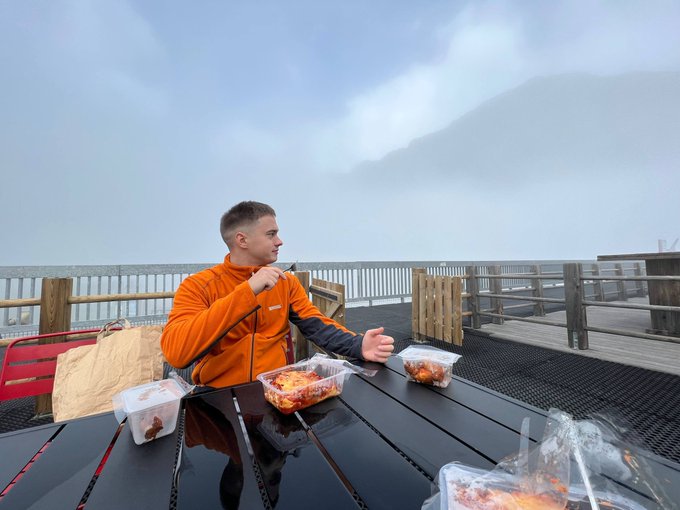 A young man in an orange fleece jacket sits at an outdoor table with takeout food containers, appearing relaxed while seemingly discussing cryptocurrency or meme coin trading dynamics on Robinhood Chain, referencing the "$CASHCAT" token's significant decline.

Note: No text, numbers, or tickers are visible in the image itself; all financial references come from the accompanying post.