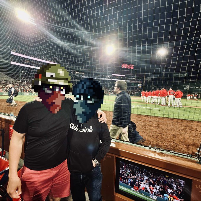 Two people posing at a baseball stadium (visible Coca-Cola and National signs) with their faces obscured by pixel art helmets resembling the Helldivers and Destiny video game characters.