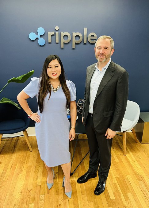 A woman in a light blue dress and a man in a gray suit pose together in front of a "ripple" logo wall, appearing to hint at a potential major XRP announcement in the accompanying post.
