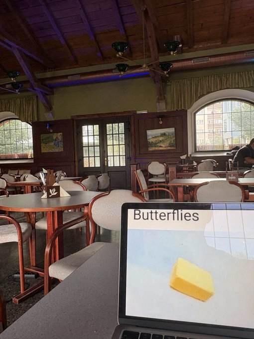 A photo taken inside a rustic, wood-beamed restaurant or cafe, with a laptop in the foreground displaying an image of a stick of butter labeled 'Butterflies'.