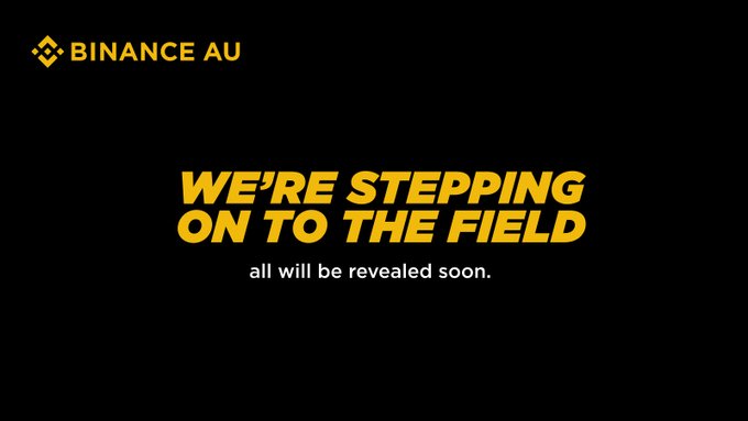 A black promotional graphic with yellow Binance AU logo and text reading 'WE'RE STEPPING ON TO THE FIELD, all will be revealed soon.'