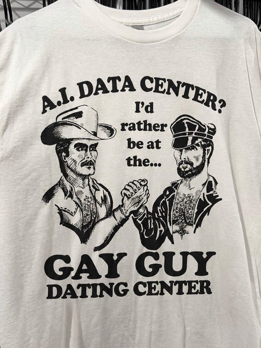 A white t-shirt featuring black ink illustrations of two cowboys arm wrestling with the humorous text 'A.I. DATA CENTER? I'd rather be at the... GAY GUY DATING CENTER'.