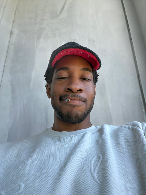 A young man wearing a red and black cap and a white textured sweatshirt takes a low-angle selfie with his eyes closed, paired with a caption about being "drained for 15,000 in ETH," suggesting the photo humorously conveys defeat after a crypto scam or loss.