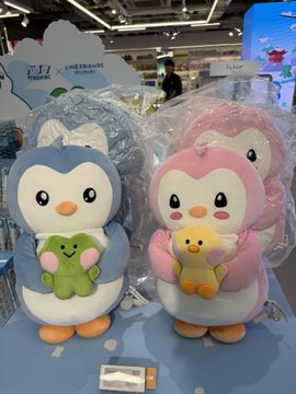 Two Pudgy Penguins plush figures, including a pink one with a small yellow chick, are wrapped in plastic packaging alongside a blue penguin, displayed at a retail stand featuring "LINE FRIENDS" branding. The image directly illustrates the official Pudgy Penguins x LINE FRIENDS collaboration merchandise mentioned in the post, showcasing the blind box collectibles that the author obtained.