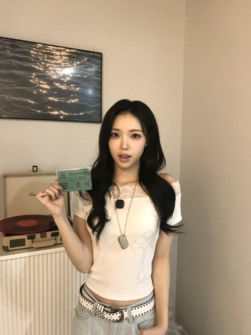 A young woman with long dark hair poses indoors, holding a Korean residence registration card ('주민등록증') next to a record player.