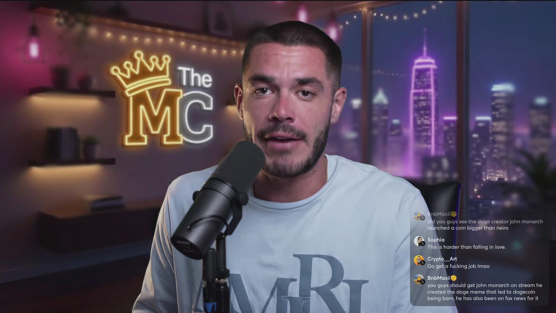 The image shows a man wearing a white shirt with "The MCR" written across his chest, standing behind a microphone. He appears to be speaking into the microphone during an online radio show or podcast. The background of the image features a city skyline at night, suggesting that they are broadcasting live from a studio in a metropolitan area.
