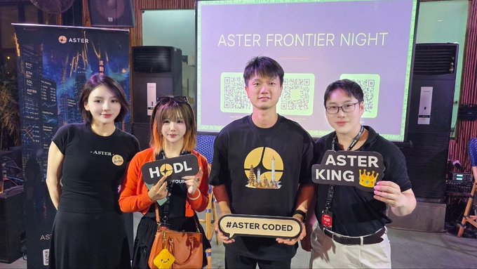 Four people pose at an "Aster Frontier Night" event, with a screen displaying the event name and QR codes behind them, holding signs that read "HODL," "ASTER KING," and "#ASTER CODED." The photo captures the Aster DEX team members and partners at the IDBW2026 conference as referenced in the post.