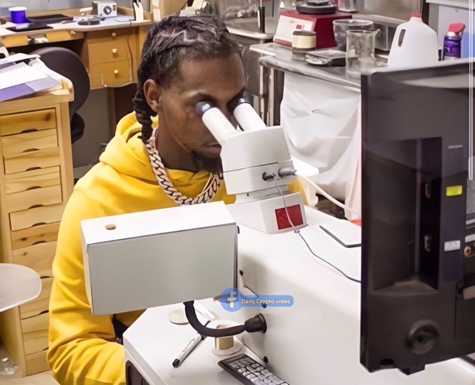 A man in a yellow hoodie looking through a microscope in what appears to be a laboratory or office setting, with a 'Daily Crypto Vibes' watermark.