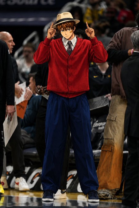 An anime-style figure with a blue and white hat, red cardigan, gray tie, and dark blue wide-leg pants stands on a basketball court, with both hands raised and index fingers pointing up near the hat.