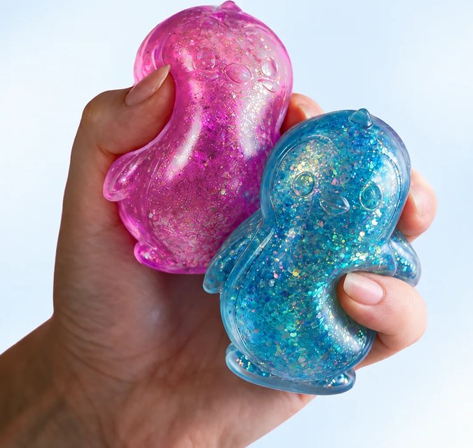 A hand holding two glitter-filled squishy toys, one pink and one blue, shaped like small creatures.