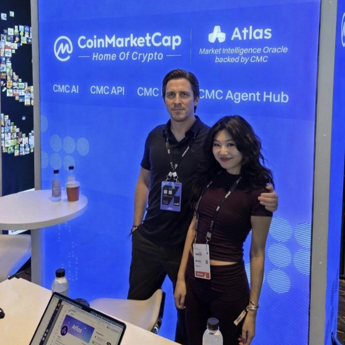 Two people posing in front of a CoinMarketCap and Atlas 'Market Intelligence Oracle backed by CMC' booth, with text showing 'CMC AI', 'CMC API', 'CMC', and 'CMC Agent Hub'.