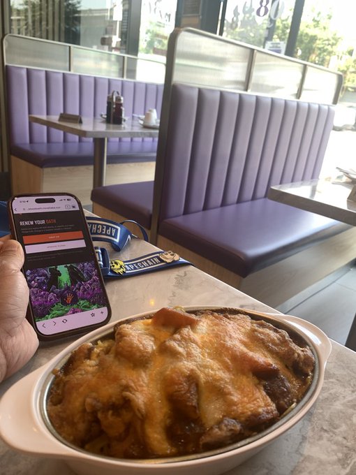 A person holds a smartphone showing a 'RENEW YOUR GFAN' interface above a bowl of food in a restaurant with purple booths.