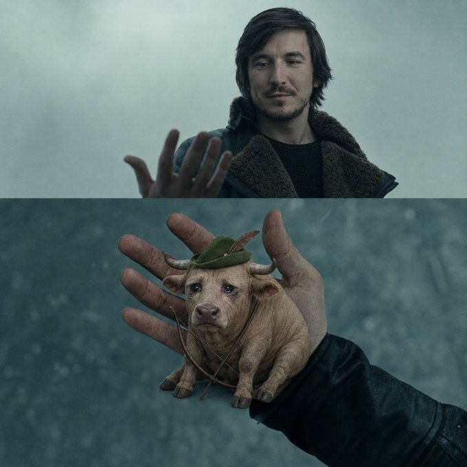 A man with dark hair and a slight smile, wearing a brown jacket with a fur collar, reaches his hand forward, while the image below shows a small pig wearing a green Robin Hood-style hat with a feather, resting in an open hand.