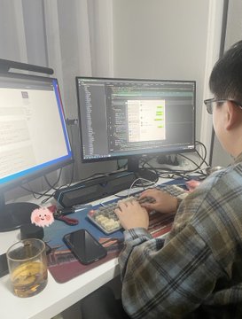 A man wearing a plaid shirt is working at his computer with two monitors in front of him, one on each side. In front of the man's desk are several electronic devices including a keyboard and mouse, as well as a cell phone that appears to be an iPhone. An empty glass sits beside the electronics on the desk, suggesting this could be a home office setup or a workstation at a co-working space. The post is about someone upgrading their Quant bot with Claude Fable 5, raking in $288K per day straight up and down on Polymarket.