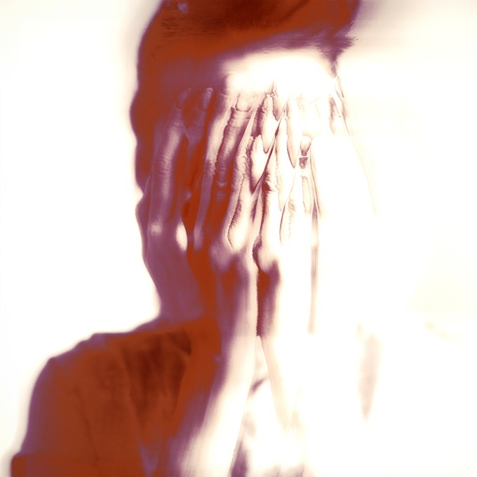 A motion-blurred, double-exposure image of a person covering their face with both hands in apparent distress, bathed in overexposed white light with reddish-orange tones, visually conveying the overwhelming struggle implied by the title "Against the Odds."