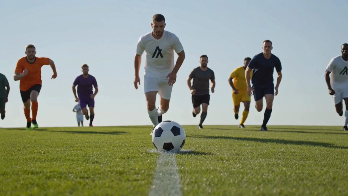 The image shows a group of men running across a soccer field, with one man kicking a soccer ball towards them. The players are wearing uniforms and appear to be engaged in an intense game or practice session. The focus of the image seems to be on the action taking place on the field rather than any additional context provided by the post.