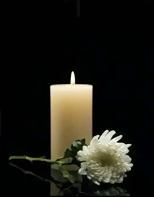A lit white candle stands beside a white chrysanthemum flower against a black background, reflecting on a glossy surface below.

This somber, memorial-style image appears to serve as a tribute image, likely commemorating the passing of "Teacher Dudu" referenced in the post, with the candle symbolizing remembrance and the white flower representing mourning and respect for his memory.