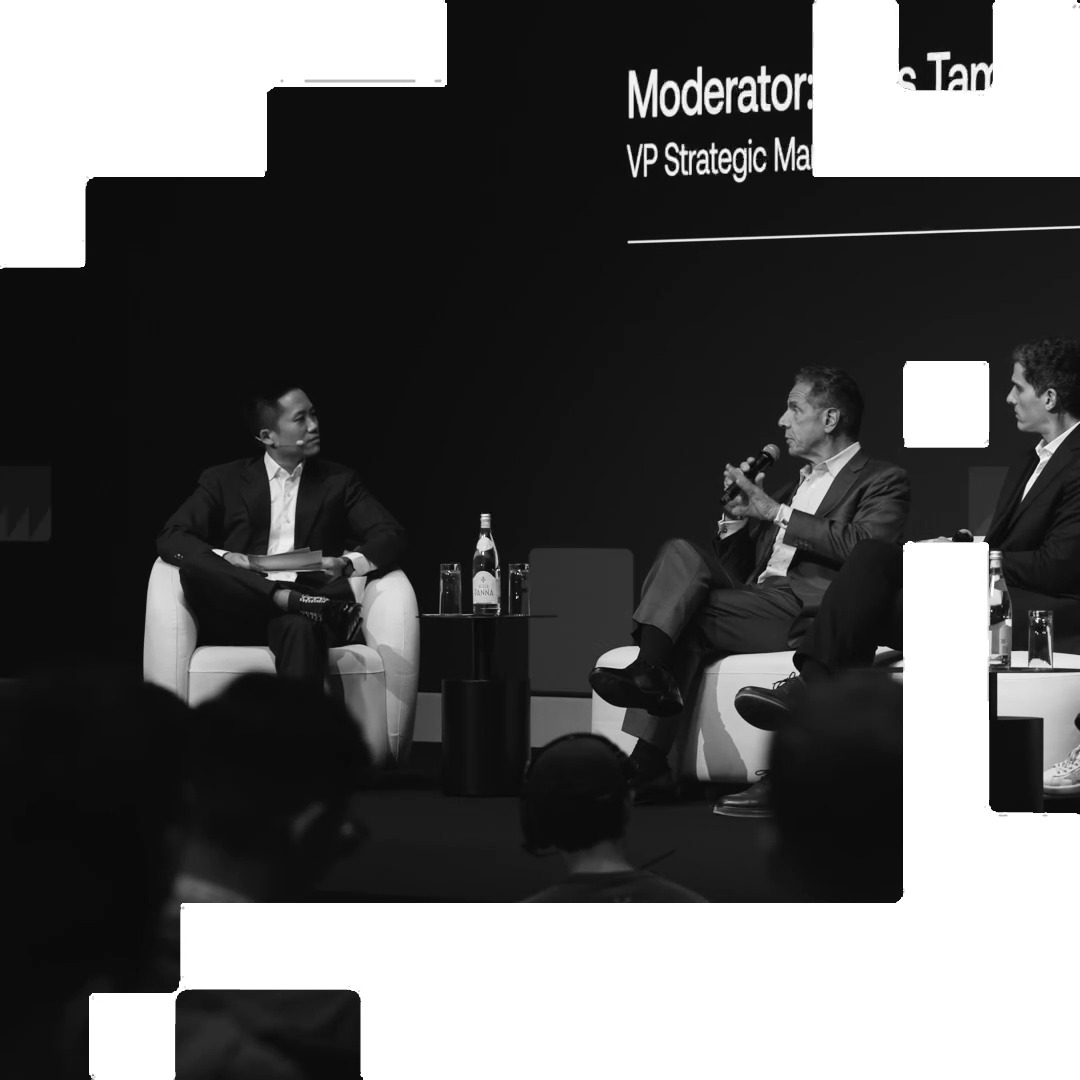 A black-and-white photo shows Andrew Cuomo, identified by the backdrop as a panelist, seated on stage in conversation during an "OKX Now" event, with another panelist listening attentively beside him. The scene captures the panel discussion referenced in the post about the OKXICE joint venture and TSV application.