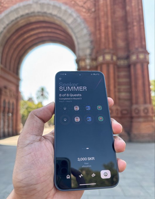 A hand holds a smartphone displaying the Seeker Summer "8 of 8 Quests Completed in Round 3" with a "3,000 SKR" allocation, set against a grand red sandstone archway. The image illustrates the post's theme of earning and compounding $SKR yield, symbolizing how small, consistent crypto rewards accumulate like compound interest—Einstein's so-called "eighth wonder of the world."