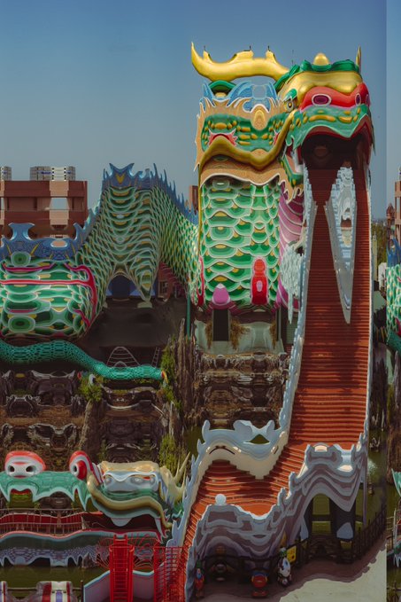A vibrant, ornate Chinese-style temple complex features two large green dragon structures with yellow horns, connected by a red staircase under a clear blue sky.
