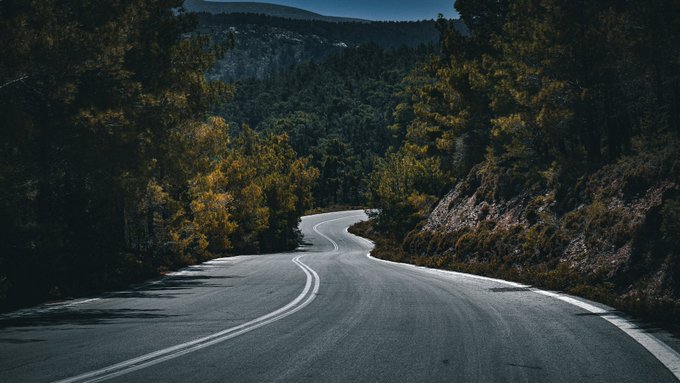 A winding asphalt road curves through a forested mountain landscape, visually embodying the title "Destiny's Road" of the NFT edition by @Sneketoshi, celebrating AEW's successful flip on secondary marketplace Objkt.