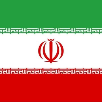 The image shows the national flag of Iran, featuring its distinctive green, white, and red horizontal stripes with the central red emblem and decorative Kufic script along the borders. The flag visually represents Iran, connecting to the news of U.S. Treasury sanctions against crypto exchanges that allegedly helped Iran's Islamic Revolutionary Guard Corps (IRGC) launder billions and evade sanctions.