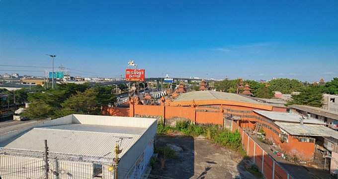 An aerial view of an urban landscape featuring a traditional Balinese-style building with distinctive red brick walls and tiered roofs, with a prominent red billboard reading "Canggu" and "Lifestyle" visible against a clear blue sky. The scene's tranquil, sun-drenched atmosphere complements the post's reflective, encouraging message about staying consistent and taking time to rest while building on CNPY Network.