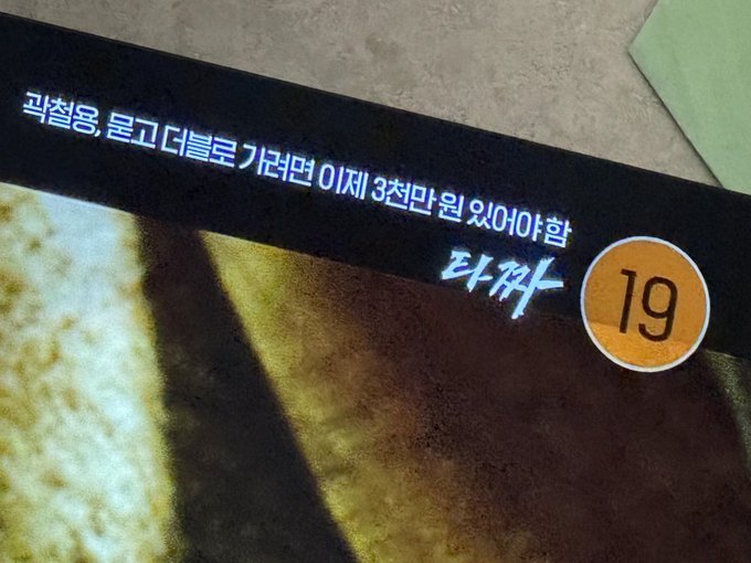 A close-up of a Korean document or certificate with white Korean text on a black background and an orange circle containing the number "19".