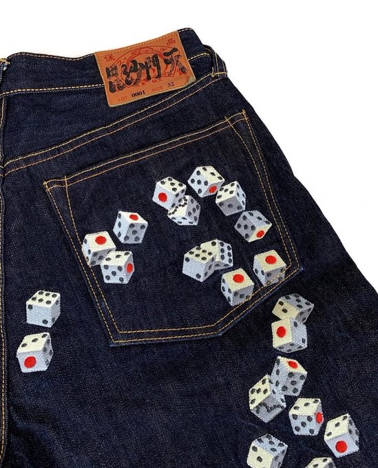 Dark denim jeans featuring a back pocket design embellished with white dice showing red and black pips scattered across the fabric.