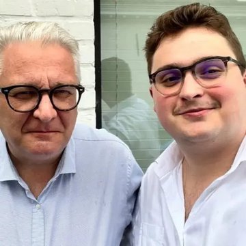 Two men wearing glasses and white button-up shirts pose for a selfie, with the younger man smiling and the older man offering a subtle smirk that complements the playful caption "Are you sure i am not a prince?"—evoking a humorous, aristocratic vibe.