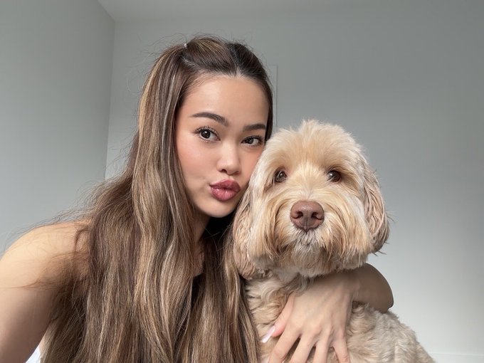 A young woman poses affectionately with a fluffy light-colored dog, likely a Labradoodle, in a close-up selfie. The caption "good dog" fits perfectly as she lovingly embraces her adorable canine companion.