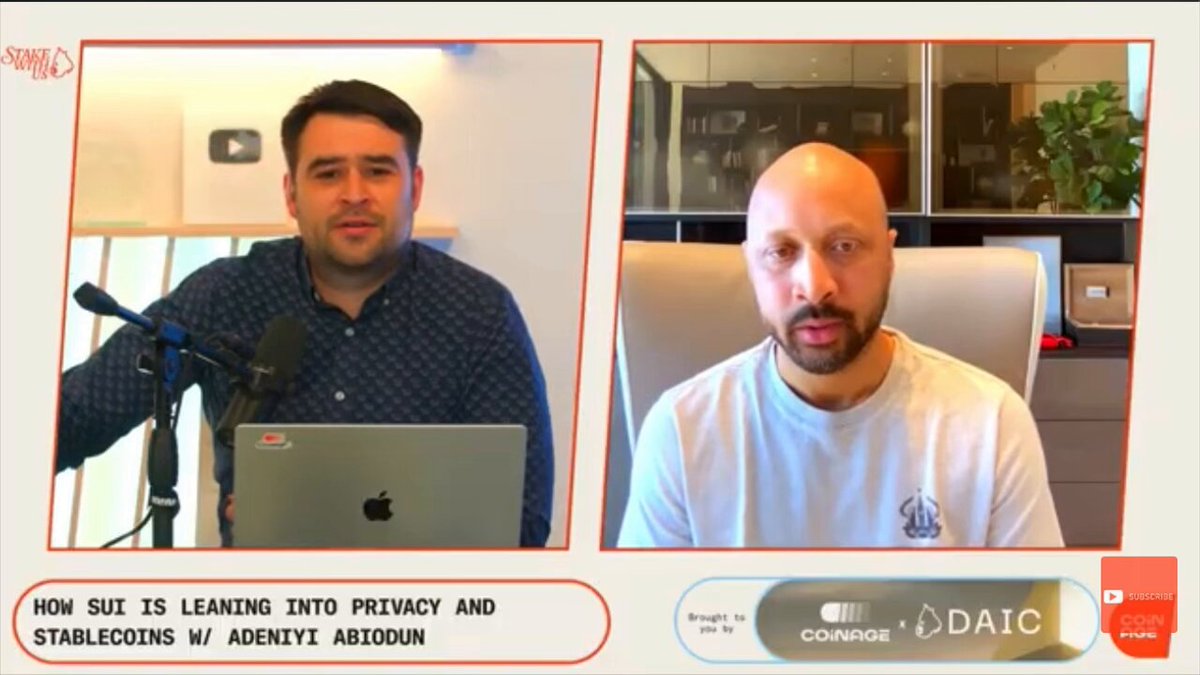 The image shows a man wearing glasses sitting behind a microphone, with another man standing next to him holding an Apple laptop computer. The two men appear to be engaged in a conversation or presentation related to cryptocurrency. In the background of the image, there is text that reads "How Suu is Leaning Into Privacy and SUI is Enduring it this year ADENIYI Says no one should have to expose their entire financial history just to send money." This message seems to be about privacy concerns in the context of cryptocurrency transactions.