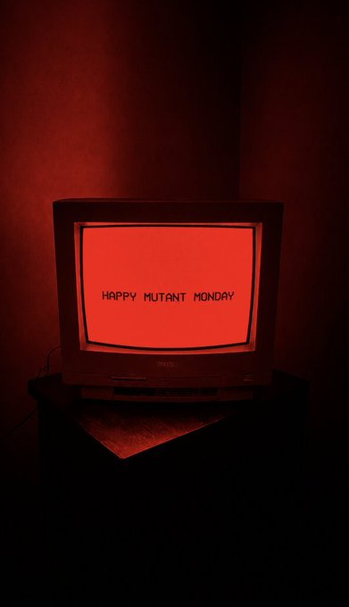 An old CRT television in a dark room with red lighting displays the text 'HAPPY MUTANT MONDAY' on its red-tinted screen.