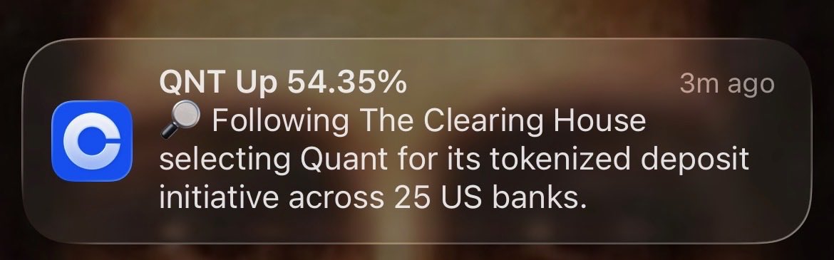 A notification from 3 minutes ago reports that QNT is up 54.35% following The Clearing House selecting Quant for its tokenized deposit initiative across 25 US banks. The image reinforces the post's claim about U.S. adoption of QNT, highlighting continued institutional validation as the XRP community awaits its own clearing breakthrough.