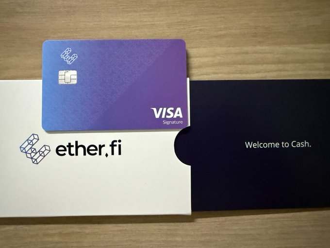 A purple-to-blue gradient Visa Signature card resting on its packaging—a white sleeve labeled 'ether.fi' and a dark envelope reading 'Welcome to Cash.'