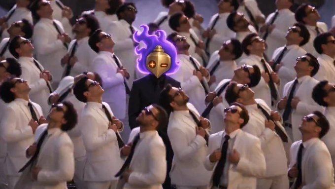 An image of a man wearing a golden Spartan-style helmet with purple flames standing among a crowd of men in white shirts and black ties, all looking upward.