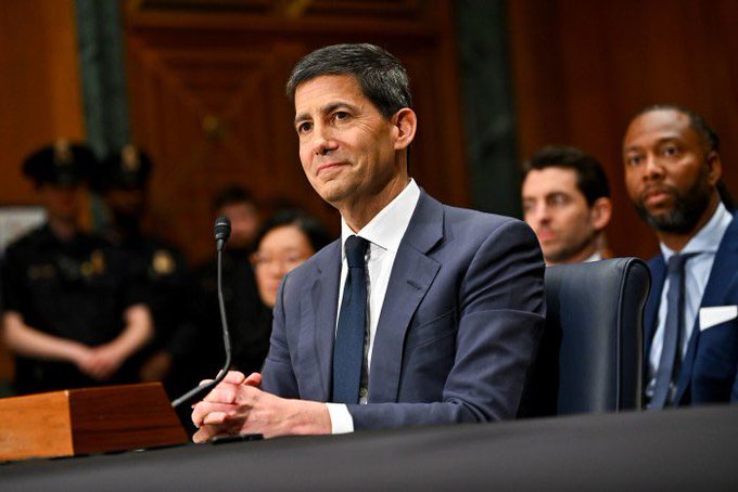 A man in a dark suit sits at a congressional hearing with his hands clasped, a microphone in front of him, while other officials and uniformed personnel are visible in the background. The image appears to be related to economic policy discussions that could have influenced the Producer Price Index (PPI) falling to 5.5%, below expectations.