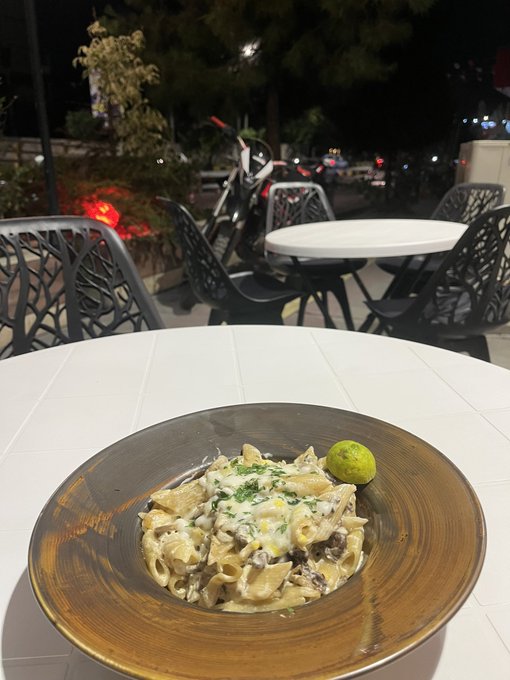 A creamy mushroom pasta dish is served in a brown ceramic bowl on a white outdoor cafe table at night, with a lime wedge on the side and a parked scooter visible in the background. The image humorously illustrates the "rugged" caption, suggesting the diner paid a steep 0.4 $SOL (Solana cryptocurrency) for what appears to be a modest portion of pasta, playing on the contrast between crypto hype and real-world value.