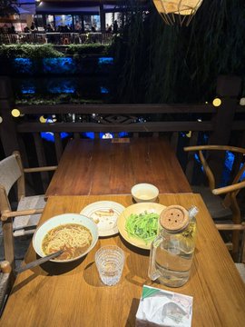 A simple meal of stir-fried noodles, bean sprouts, and fresh greens sits on a wooden table at a dimly lit restaurant, complementing the post's reflection on an inexpensive dinner with a Beijing neighbor.