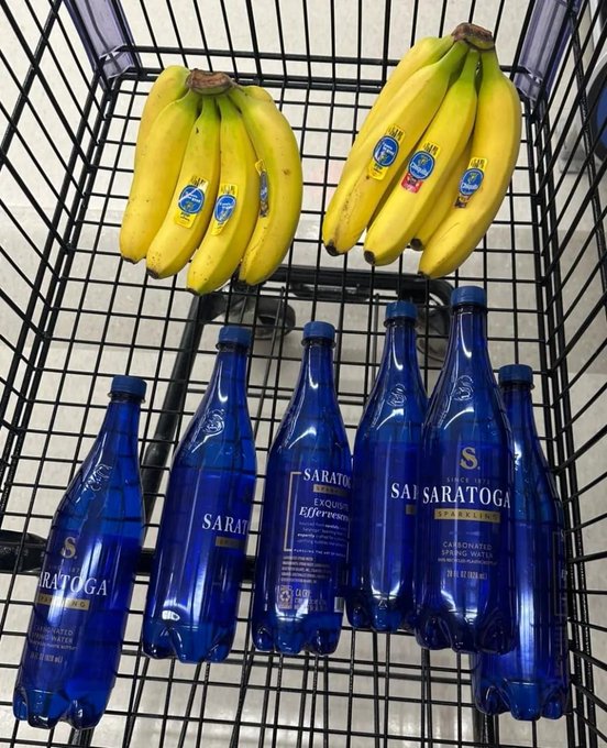 A wire shopping basket containing bunches of yellow bananas and several blue bottles of Saratoga sparkling water.