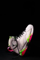 A white Air Jordan sneaker with neon green and pink accents is displayed against a black background.