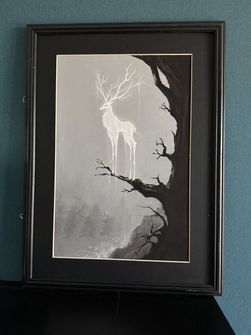 A framed black-and-white artwork depicts an ethereal, glowing deer with elongated, melting legs standing on the branch of a dark, gnarled tree against a misty forest backdrop.