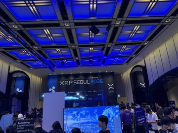 An interior view of the XRP SEOUL 2026 conference venue shows a large blue-lit ceiling, a digital display reading 'XRP SEOUL 2026', and attendees gathered below.