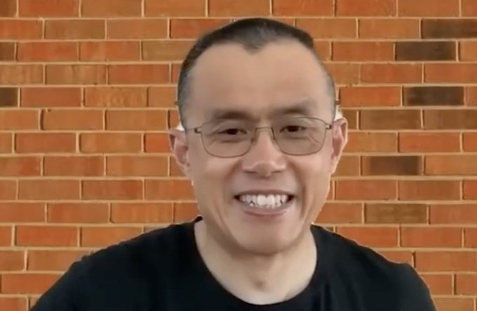 A man with short hair and glasses, smiling, stands against a brick wall background, appearing to be CZ, the founder of Binance, discussing his reflections on his career and the importance of learning about law, regulation, and politics.