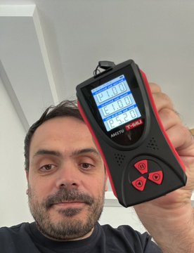 A selfie of a bearded man holding up a red and black electronic device with multiple digital displays and buttons, branded 'MOTOP'.
